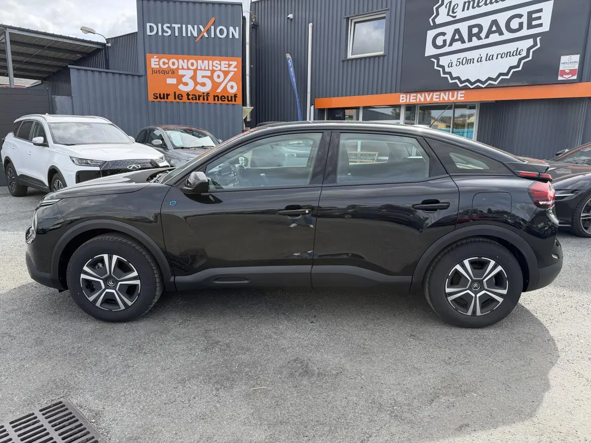 Profil droit d'une Citroën C4 électrique noire 2025 avec inserts noir brillant, stationnée devant un garage.