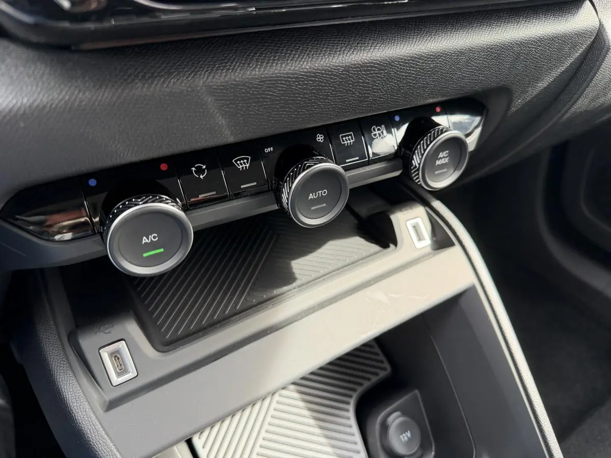 Gros plan sur la console centrale de la Citroën C4 ë-136 2025, montrant les commandes de climatisation et une prise USB.