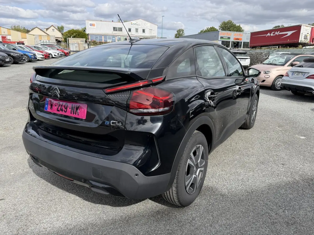 Vue 3/4 arrière droite d'une Citroën C4 ë-136 noire avec inserts noir brillant, stationnée en extérieur.