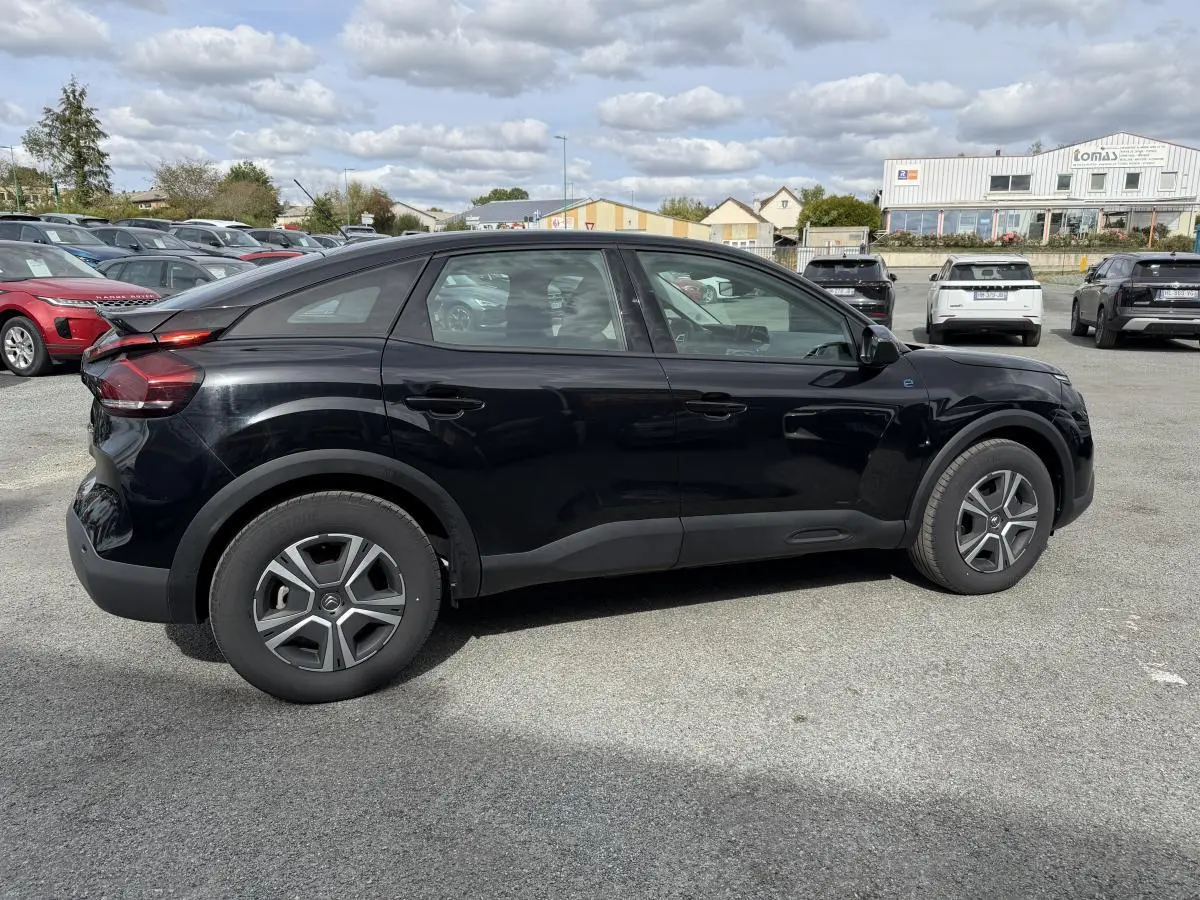 Profil droit d'une Citroën C4 électrique noire avec inserts noir brillant sur un parking extérieur.