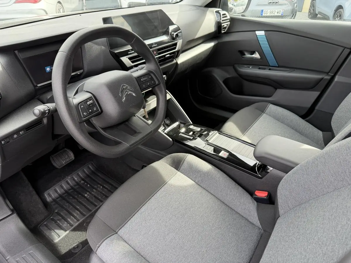 Intérieur avant droit de la Citroën C4 ë-136 2025, tableau de bord noir avec inserts bleus et sièges tissu gris.
