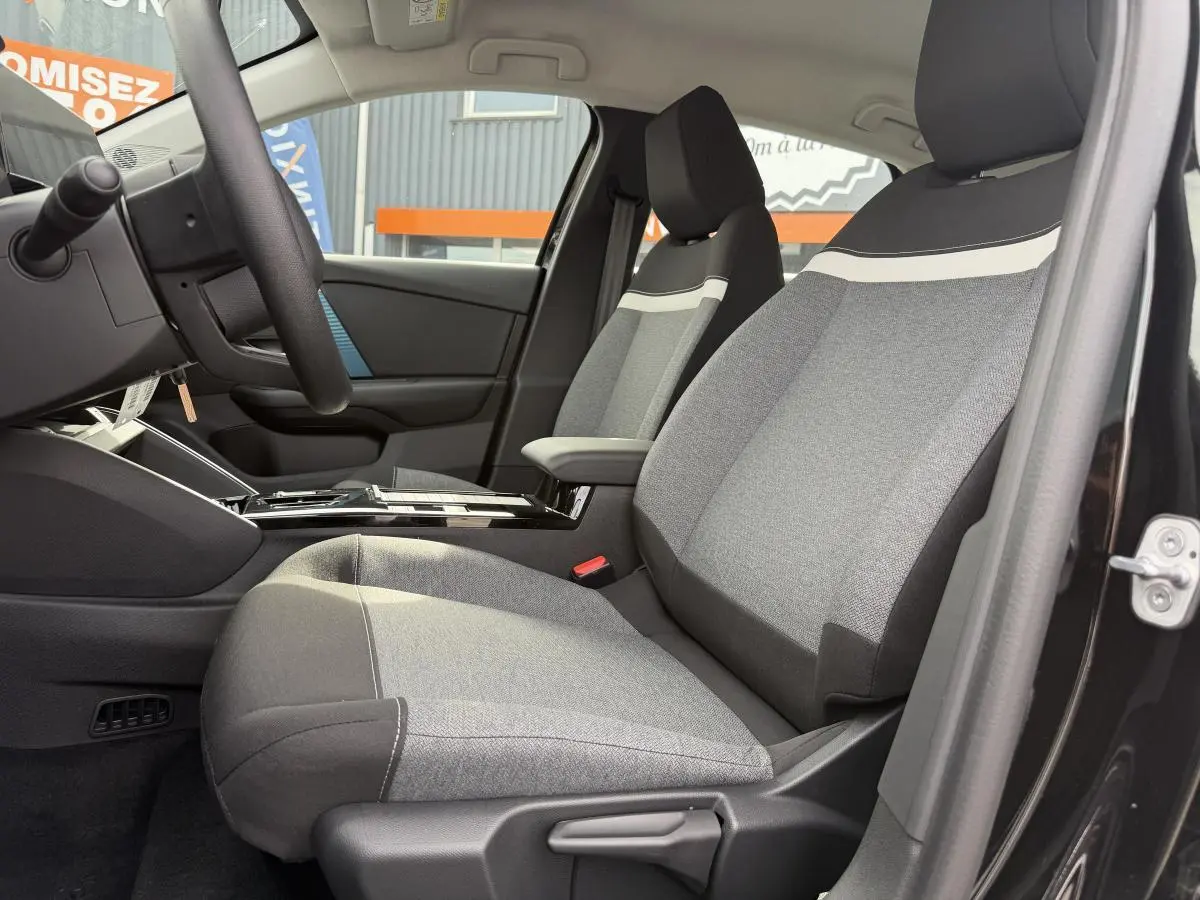 Vue intérieure côté conducteur de la Citroën C4 ë-136 2025, sièges tissu gris avec bande blanche, porte noire ouverte.