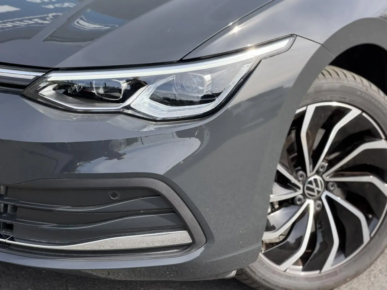 Gros plan sur l'avant droit de la Volkswagen Golf VIII gris Urano, mettant en valeur le phare LED et la jante alliage 17 pouces.