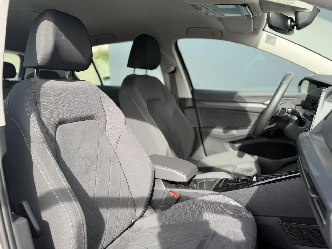 Vue intérieure côté conducteur de la Volkswagen Golf VIII Style 2024 avec sièges microfleece gris et accoudoir central.