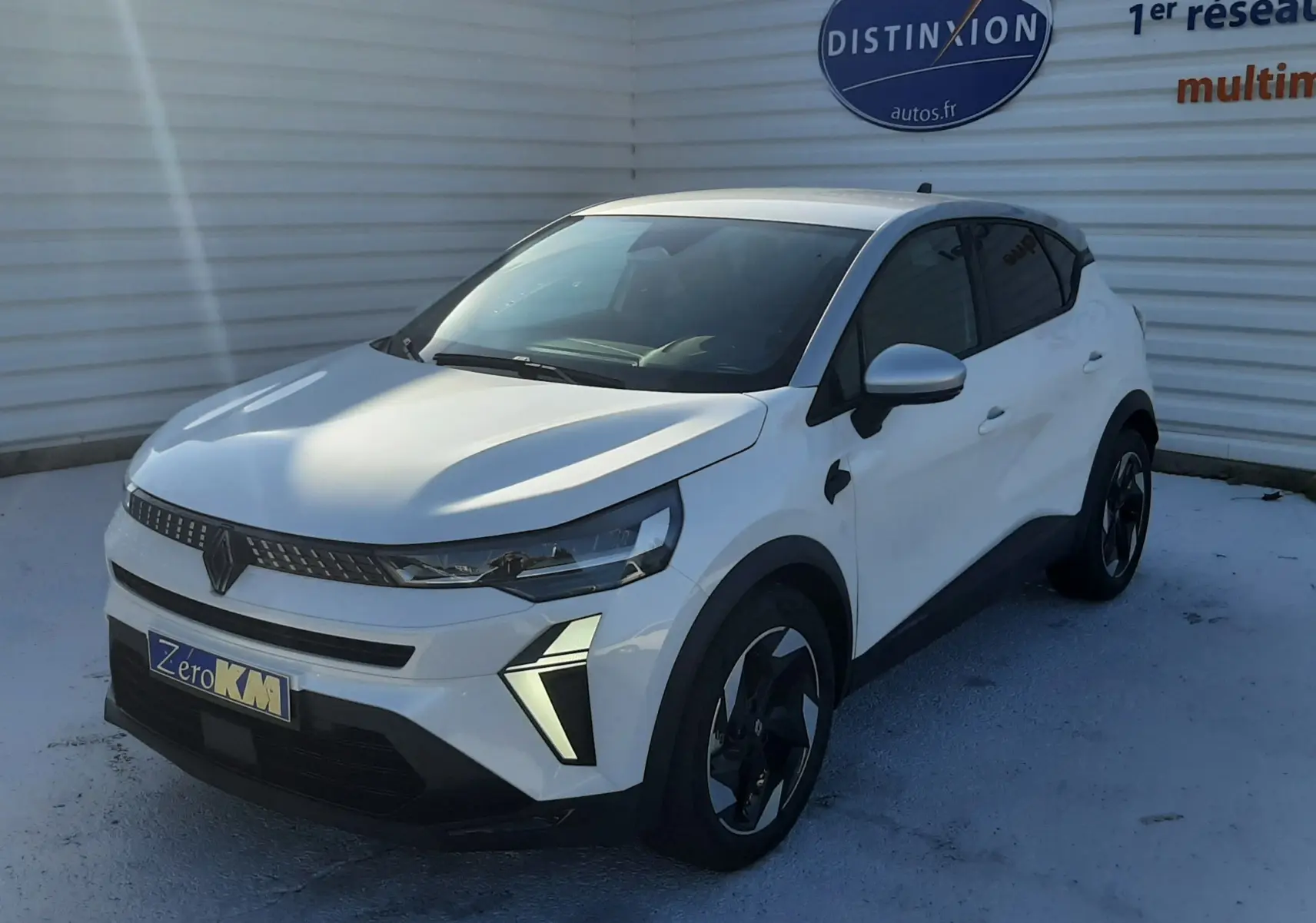 Renault Captur 2025 blanc nacré toit gris en 3/4 avant droit, avec feux LED et jantes noires distinctives.