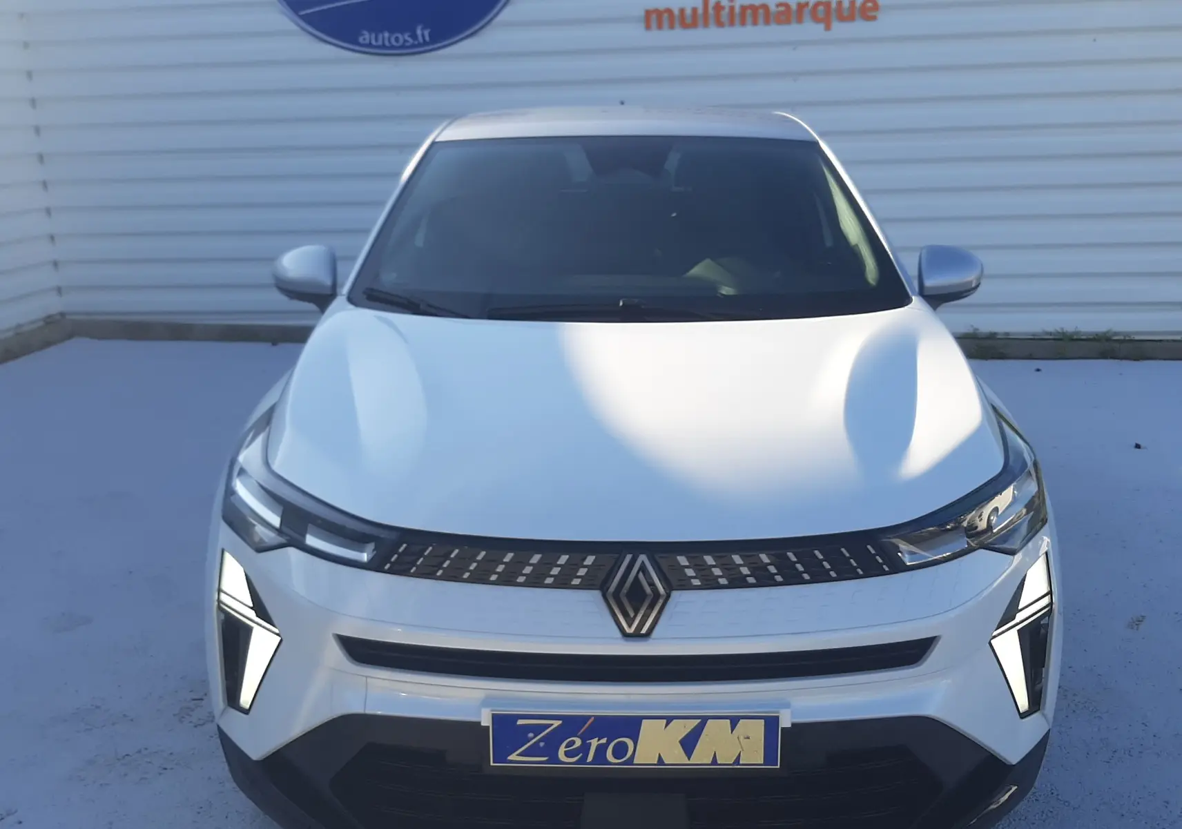 Vue avant d'un Renault Captur blanc nacré avec toit gris Highland, mettant en valeur ses feux LED et calandre moderne.