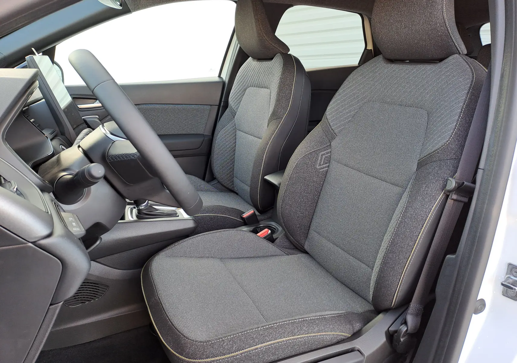 Intérieur avant droit du Renault Captur 2025, sièges tissu gris avec coutures contrastantes et volant visible.
