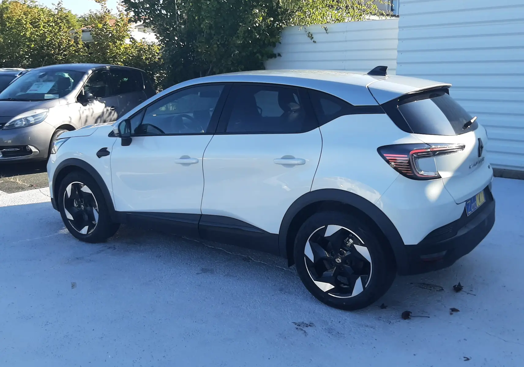 Renault Captur 2025 blanc nacré avec toit gris Highland, vue 3/4 arrière côté gauche, jantes noires distinctives.