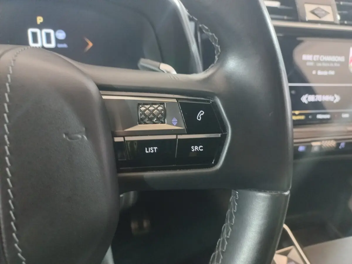 Gros plan sur les commandes gauche du volant cuir noir du DS7 Crossback 2021 avec écran tactile en arrière-plan.