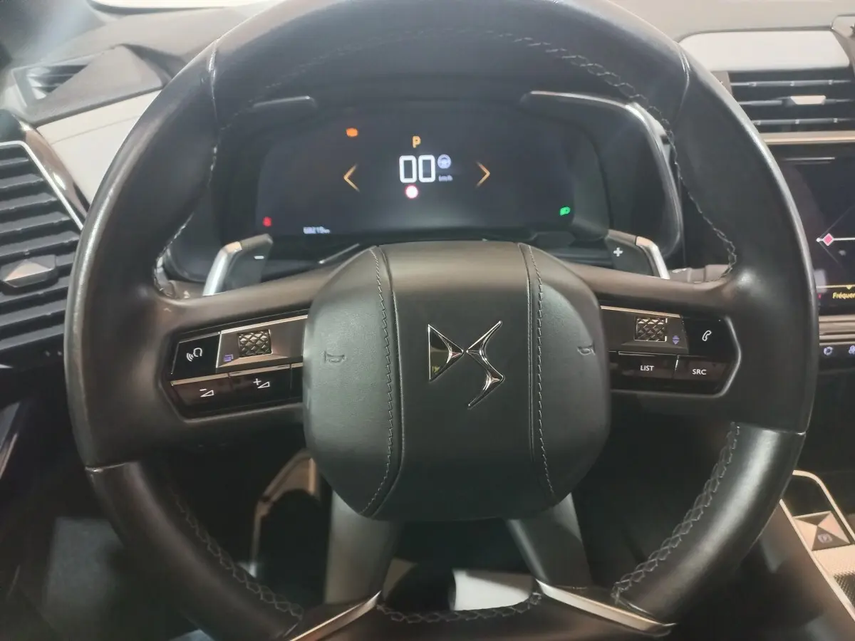 Vue rapprochée du volant cuir noir multifonctions du DS7 Crossback avec tableau de bord numérique en arrière-plan.