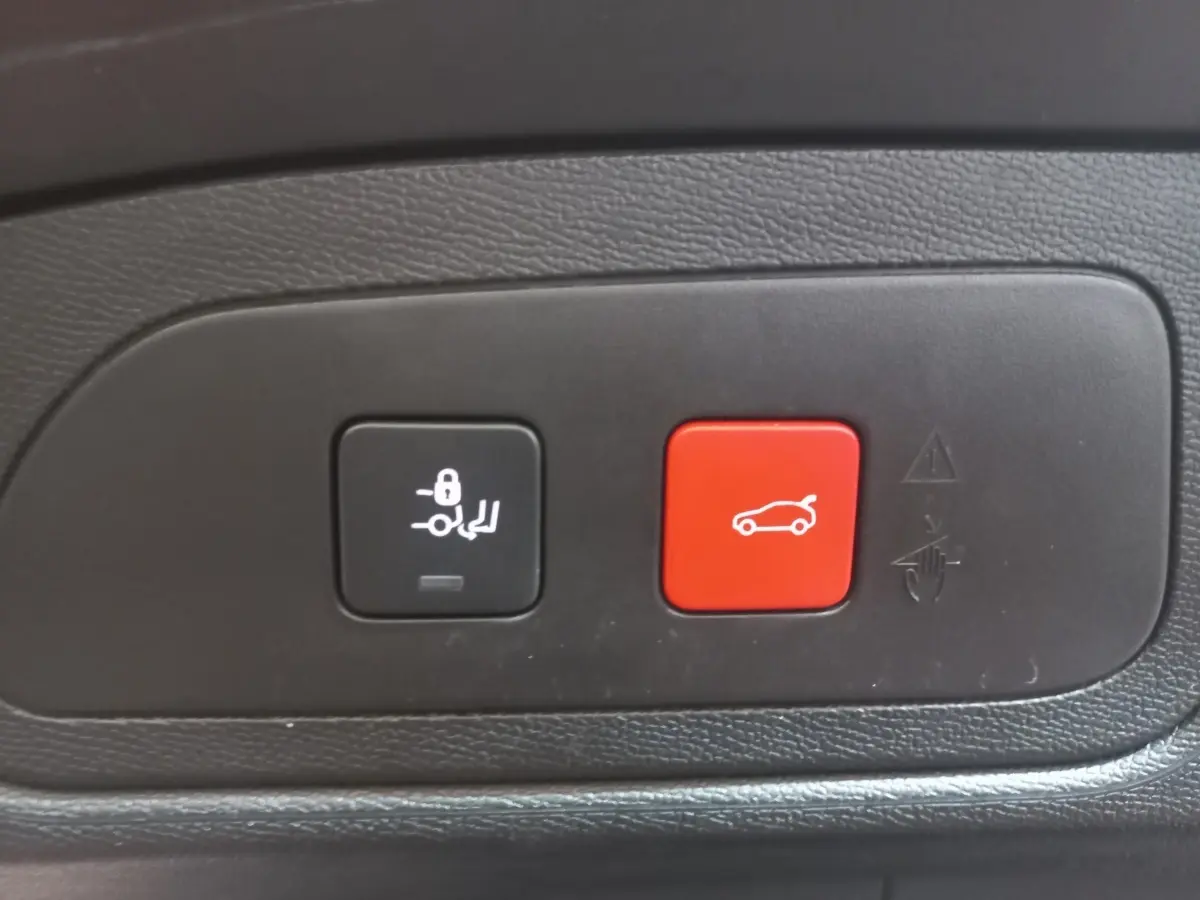Gros plan sur les boutons de commande du coffre électrique, noir et rouge, intérieur d’un DS7 Crossback gris foncé.