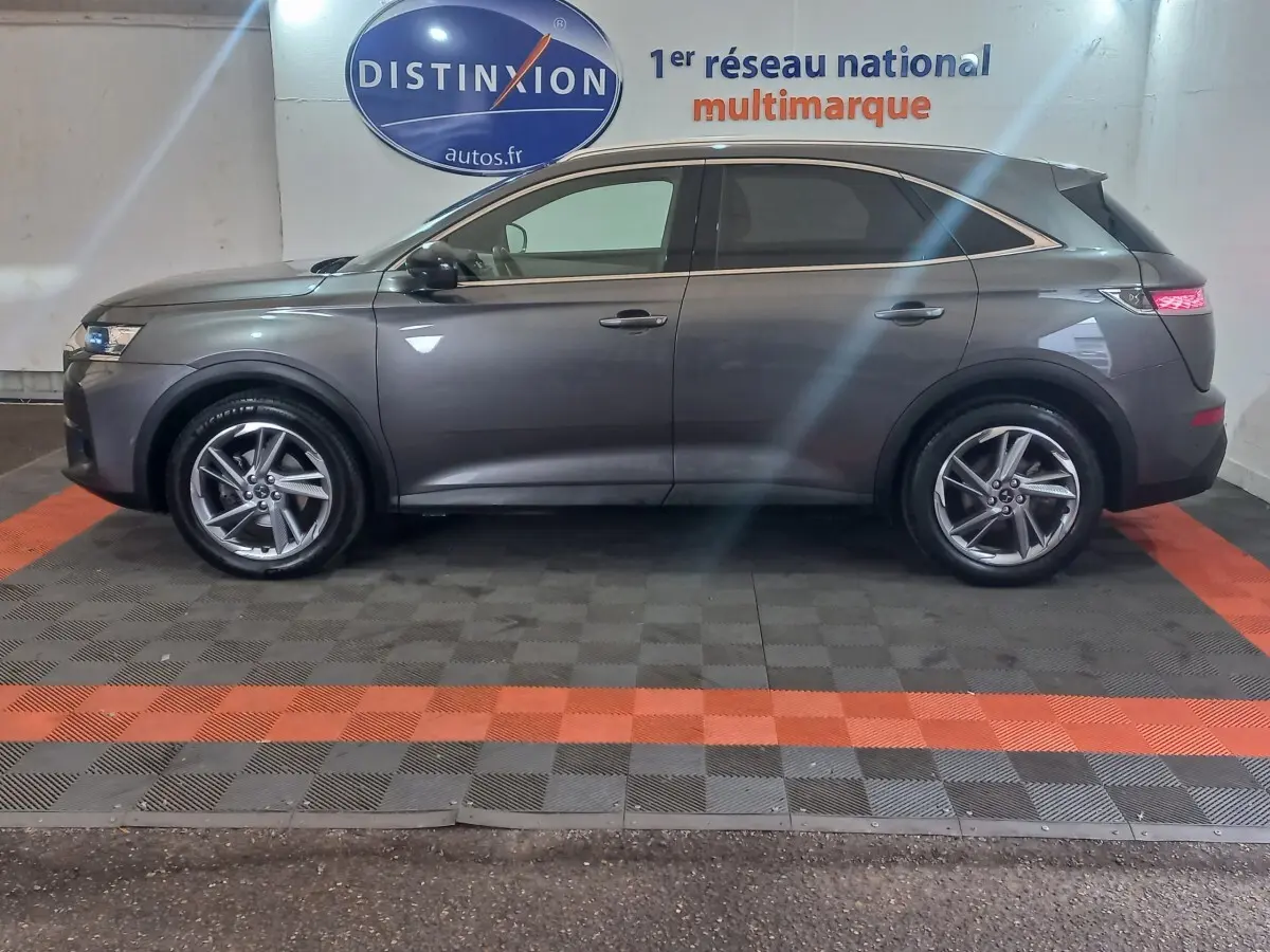 Vue latérale droite d'un DS7 Crossback gris foncé garé en intérieur avec jantes alliage et feux arrière allumés.