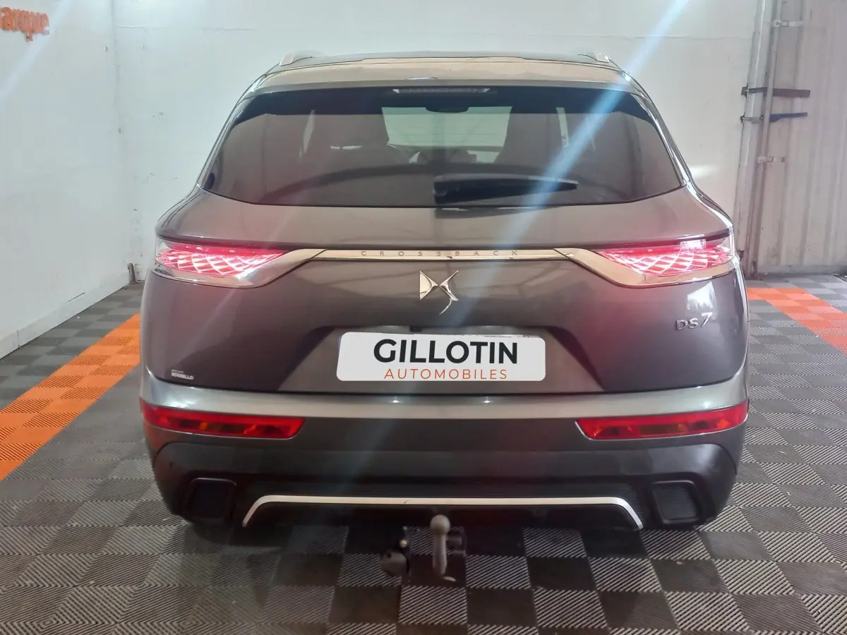 Vue arrière d'un DS7 Crossback gris foncé avec feux LED allumés et attelage visible en intérieur showroom.