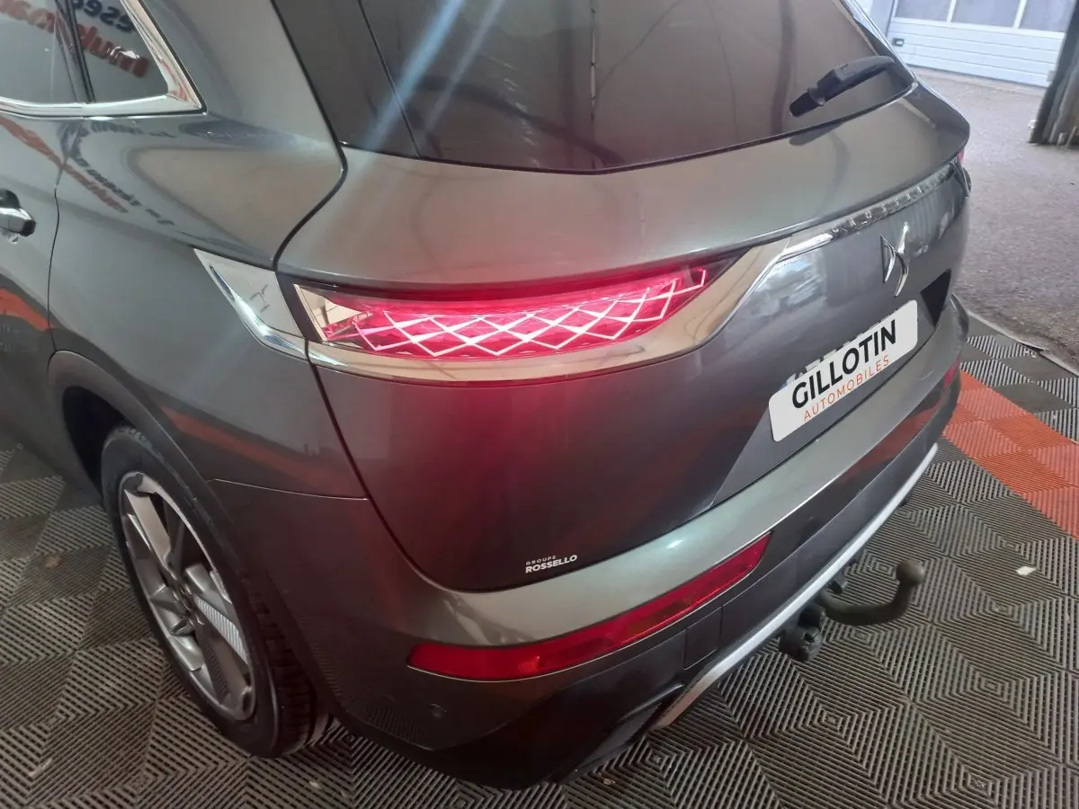 Vue 3/4 arrière droite du DS7 Crossback gris foncé avec feux arrière allumés et attelage visible.