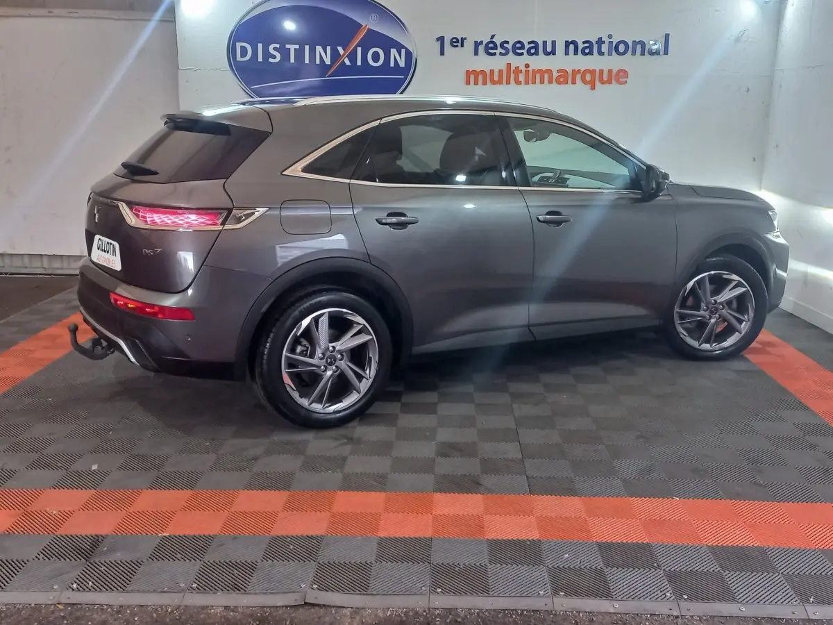 Vue de profil côté gauche du DS7 Crossback gris foncé 2021 avec feux arrière allumés et jantes alliage distinctives.