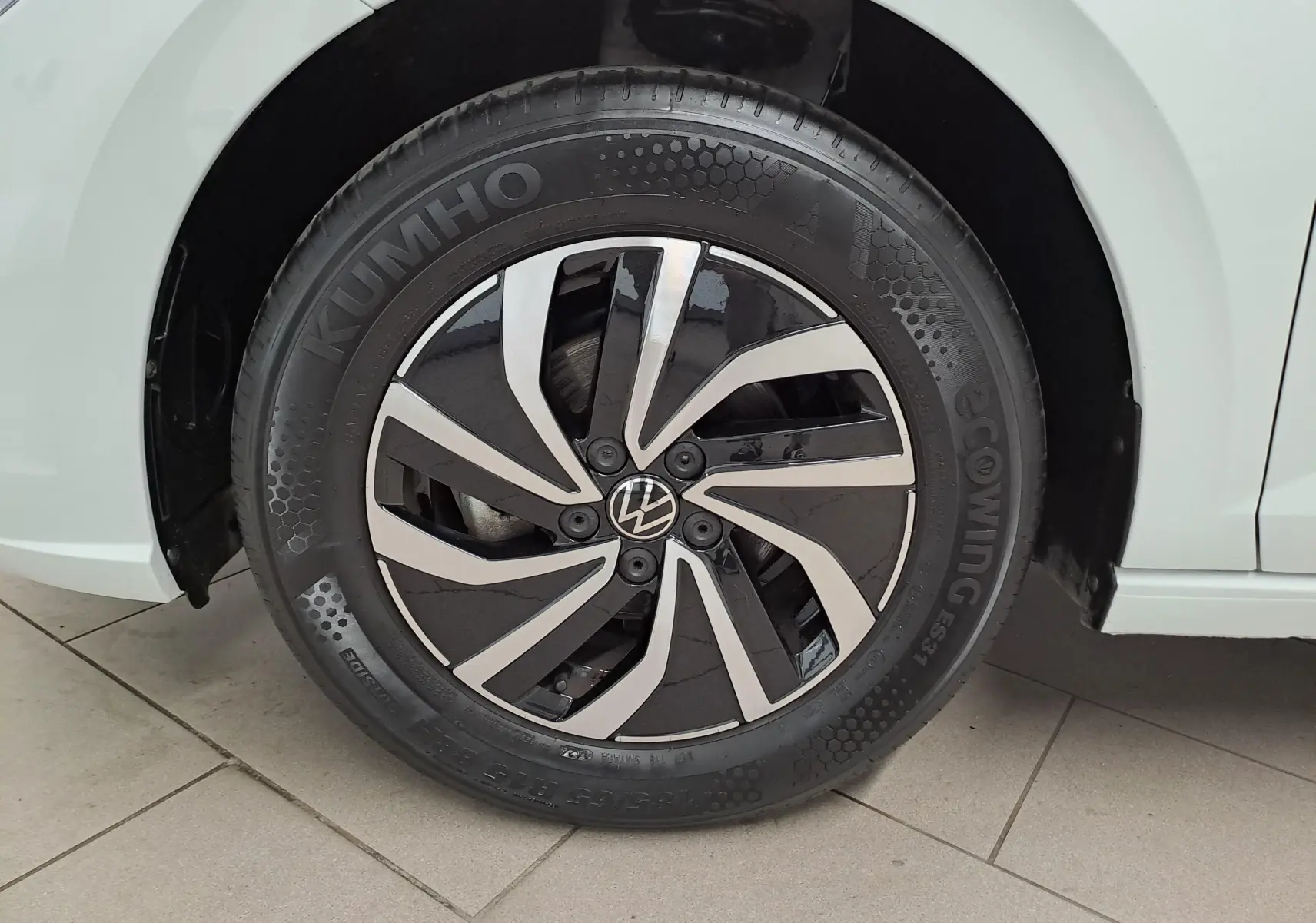 Gros plan sur la roue avant gauche d'une Volkswagen Polo blanche, avec jante alliage noire et argentée au design moderne.