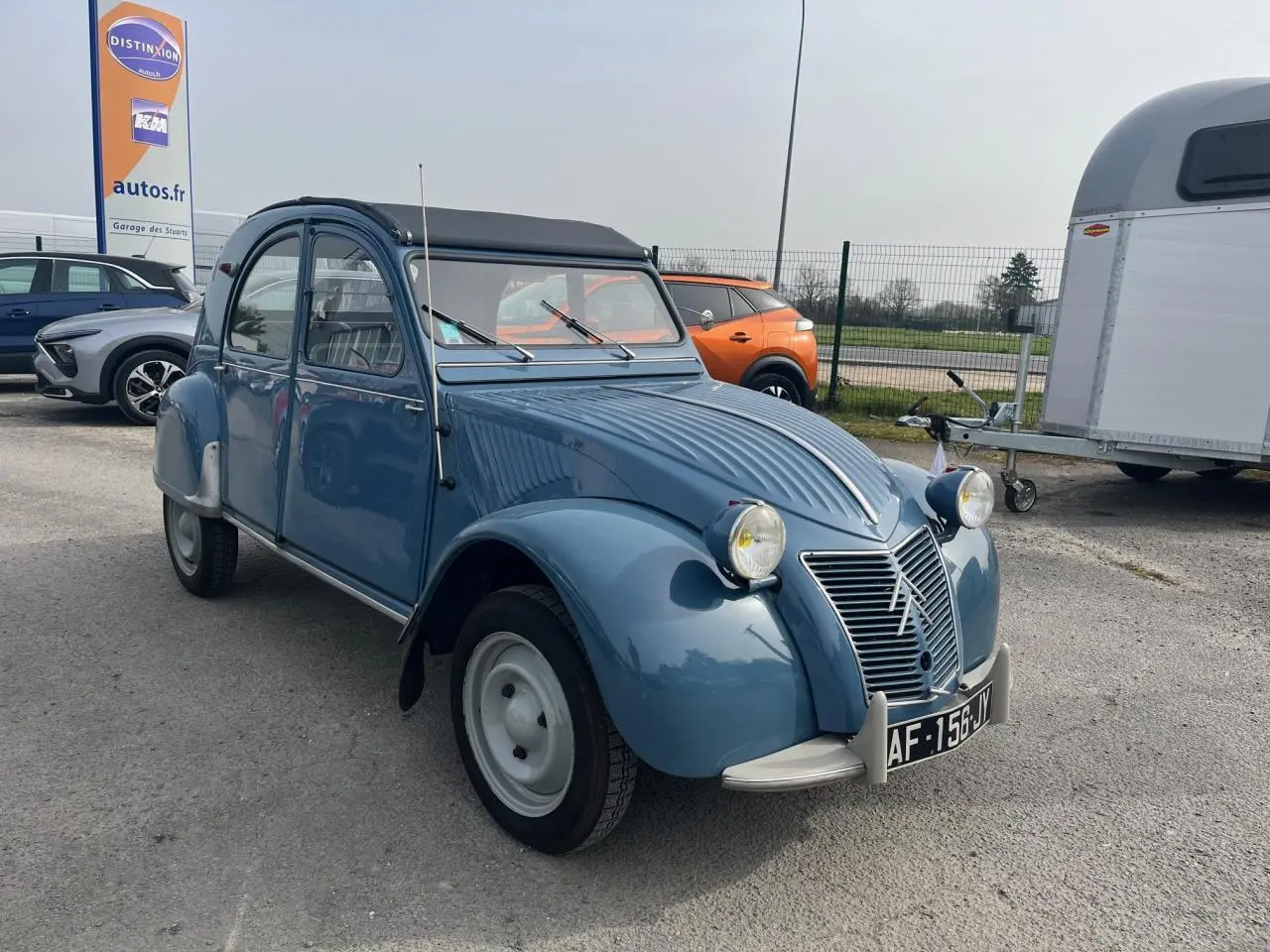 Citroën 2 CV bleu clair vue 3/4 avant droit, toit souple noir et phares ronds caractéristiques.