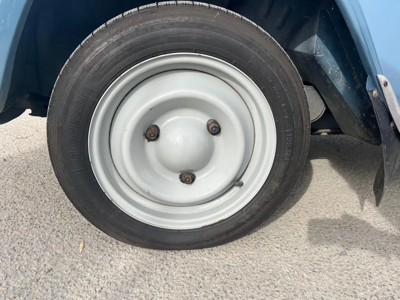 Gros plan sur la roue avant droite blanche d’une Citroën 2CV bleu clair de 1960, avec pneu Michelin visible.