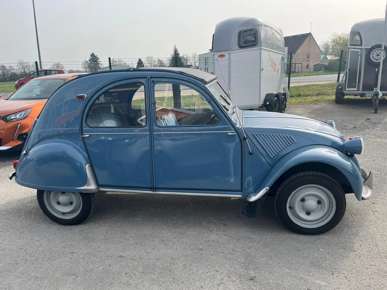 Profil côté gauche d'une Citroën 2CV bleu clair de 1960 avec toit ouvrant en toile partiellement replié.