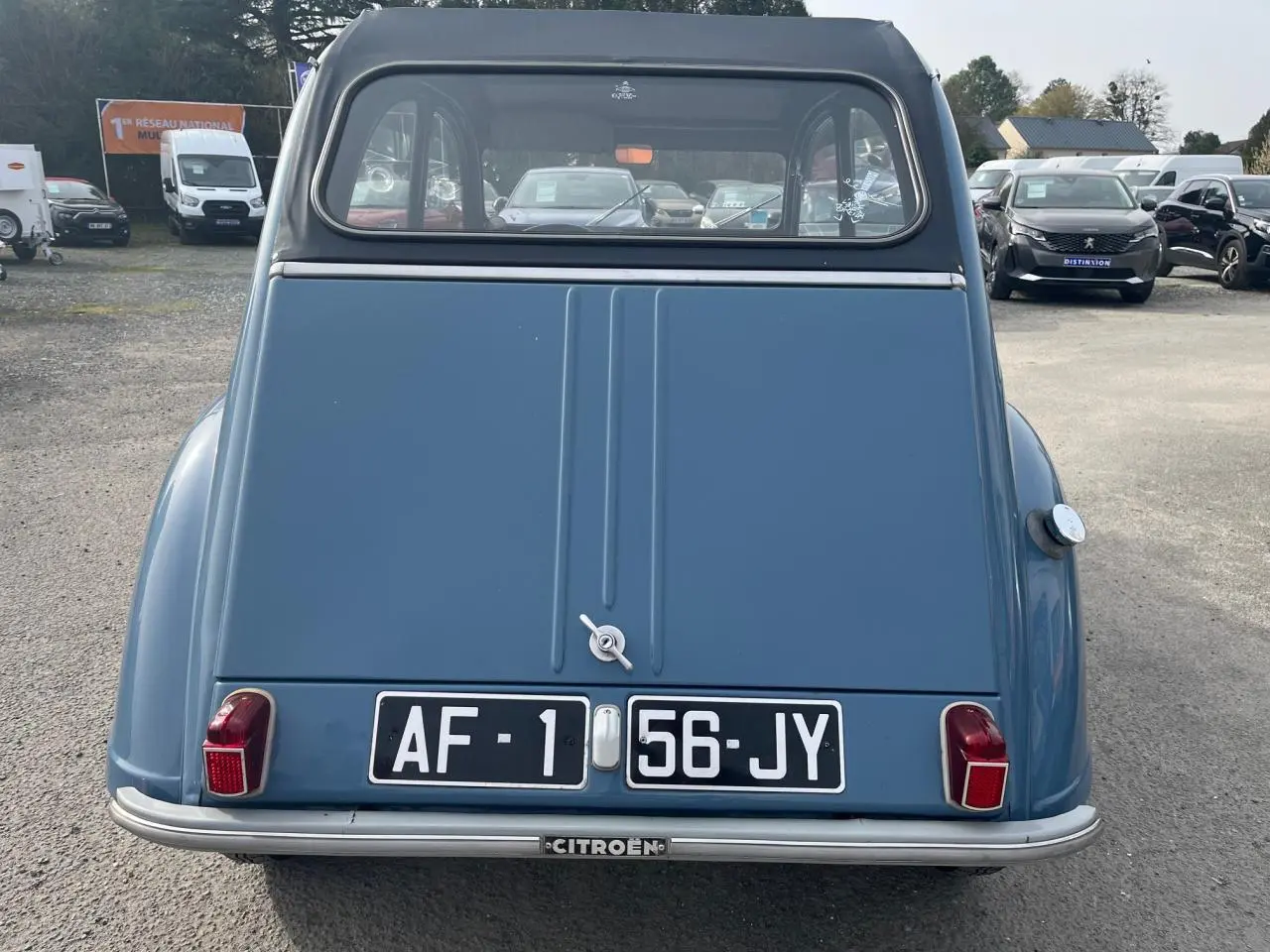 Vue arrière d'une Citroën 2CV bleu clair de 1960, avec ses feux rouges caractéristiques et plaque d'immatriculation noire.