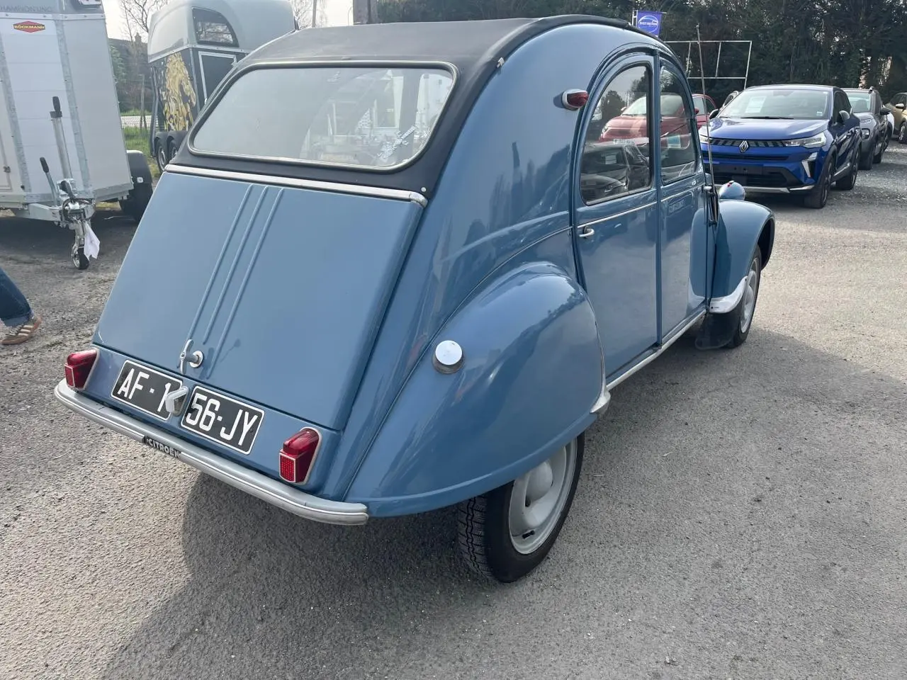Vue 3/4 arrière droite d'une Citroën 2CV bleu clair de 1960 avec toit souple noir et plaques d'immatriculation françaises.