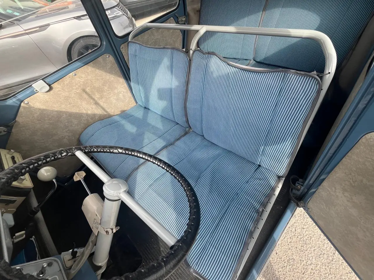 Intérieur de Citroën 2 CV 1960 bleu clair, vue plongeante sur siège avant à coussins rayés et volant fin noir.