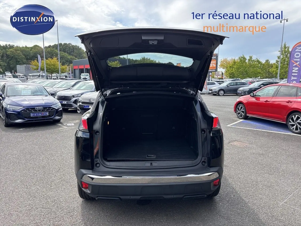 Vue arrière de la Peugeot 3008 HYBRID noire métal 2024 avec coffre ouvert sur parking multimarque.