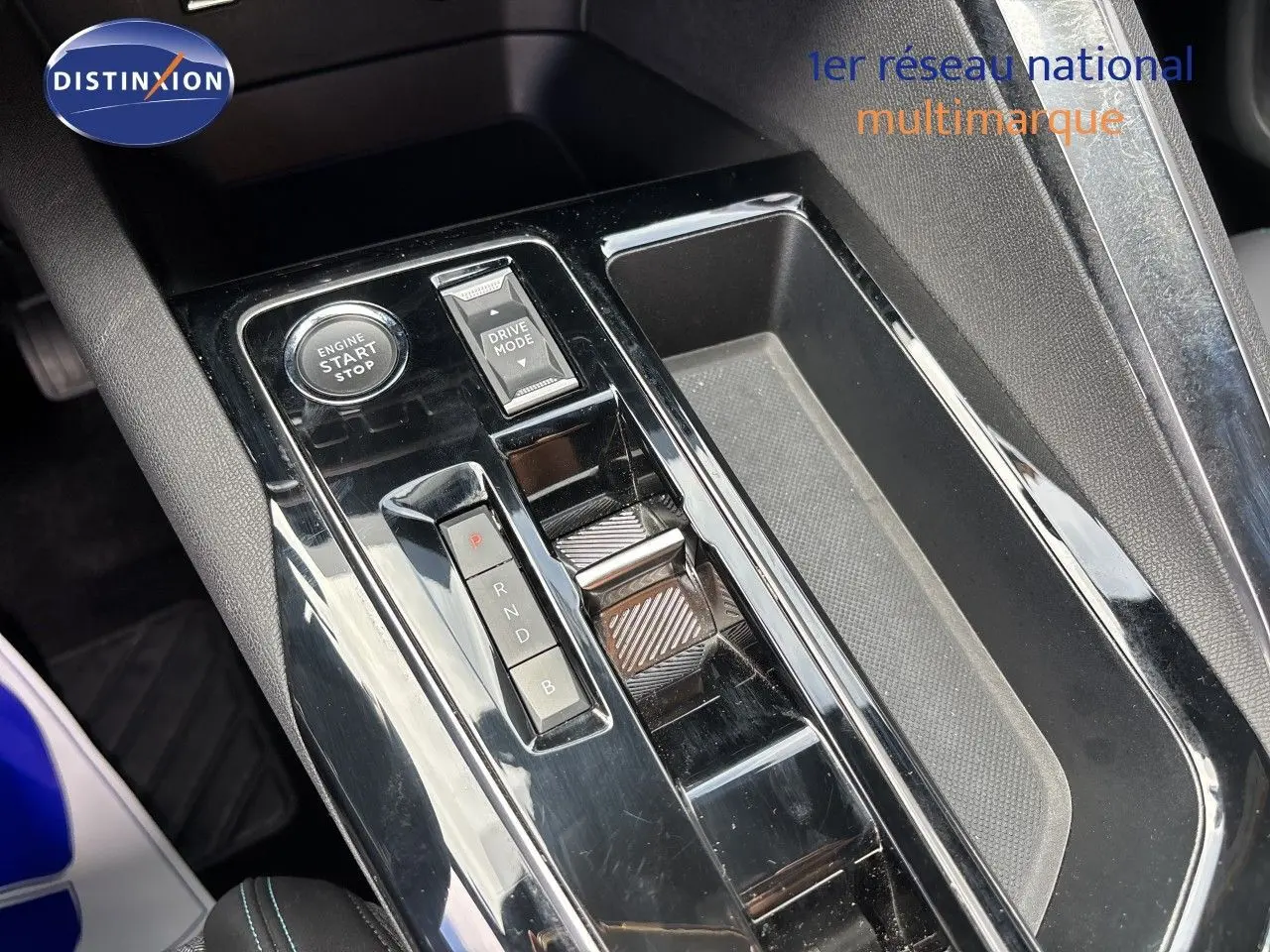 Gros plan sur la console centrale noire brillante du Peugeot 3008 Hybrid 180ch avec bouton start/stop et sélecteur de mode de conduite.
