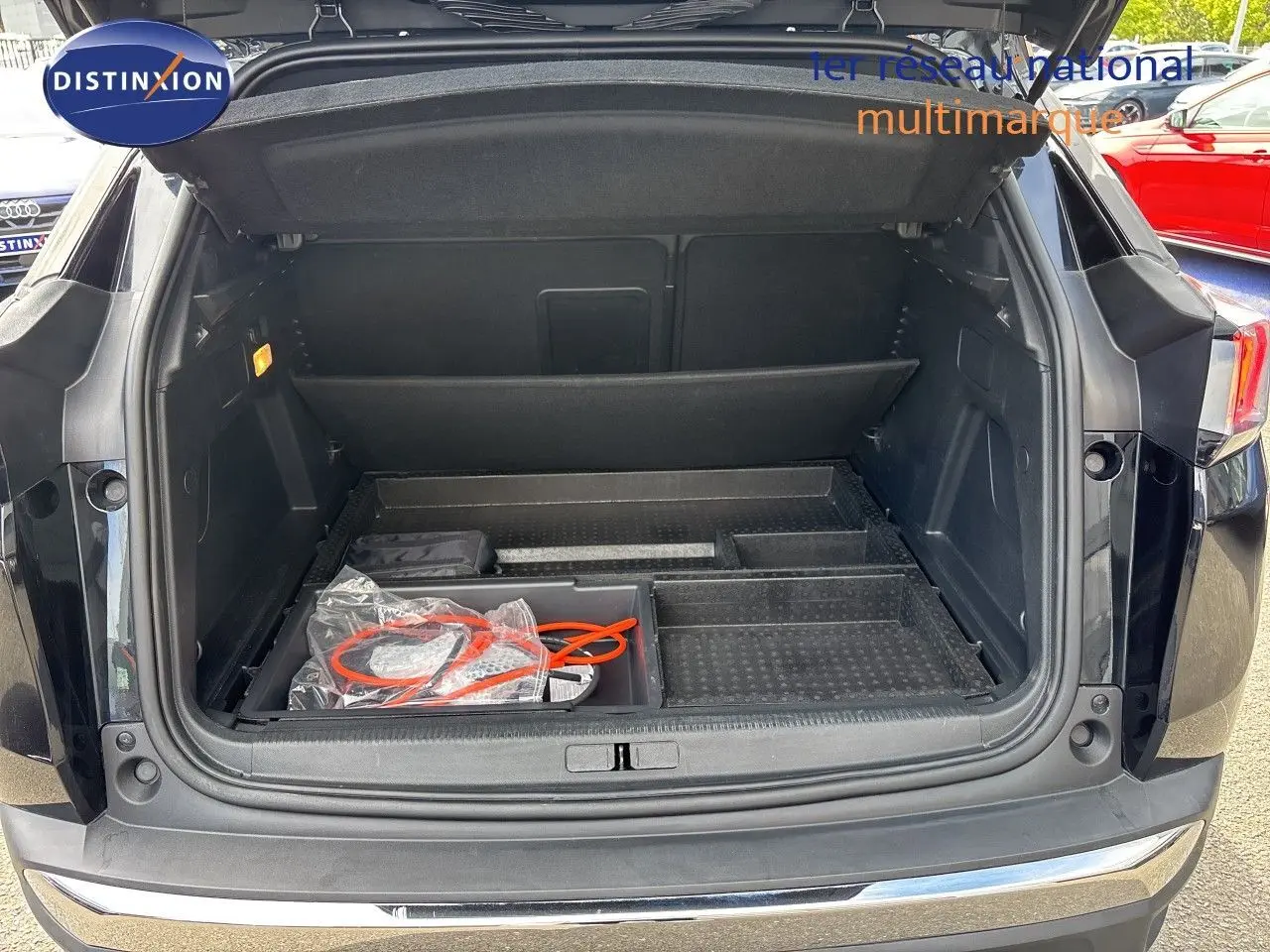 Coffre ouvert d’un Peugeot 3008 HYBRID noir métal, vue arrière montrant l’espace de rangement et câbles de recharge.