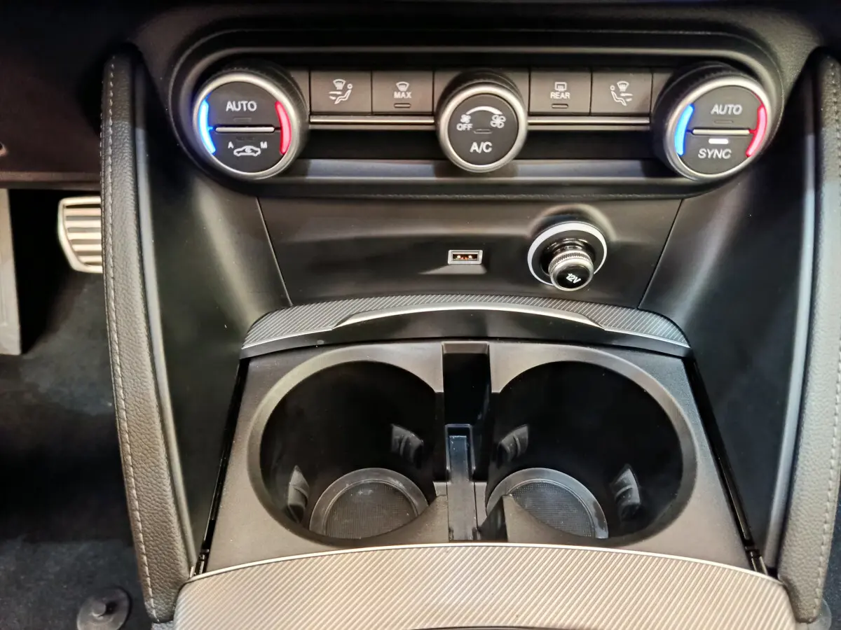 Gros plan sur la console centrale de l'Alfa Romeo Stelvio 2024 gris foncé, avec commandes climatisation et prises USB visibles.