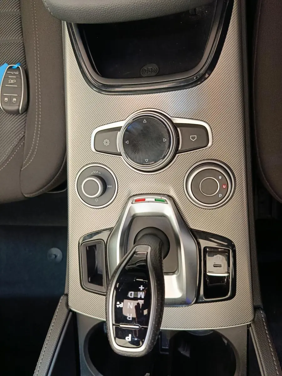 Vue plongeante sur la console centrale gris foncé de l'Alfa Romeo Stelvio 2024 avec levier de vitesse automatique et molette de contrôle.