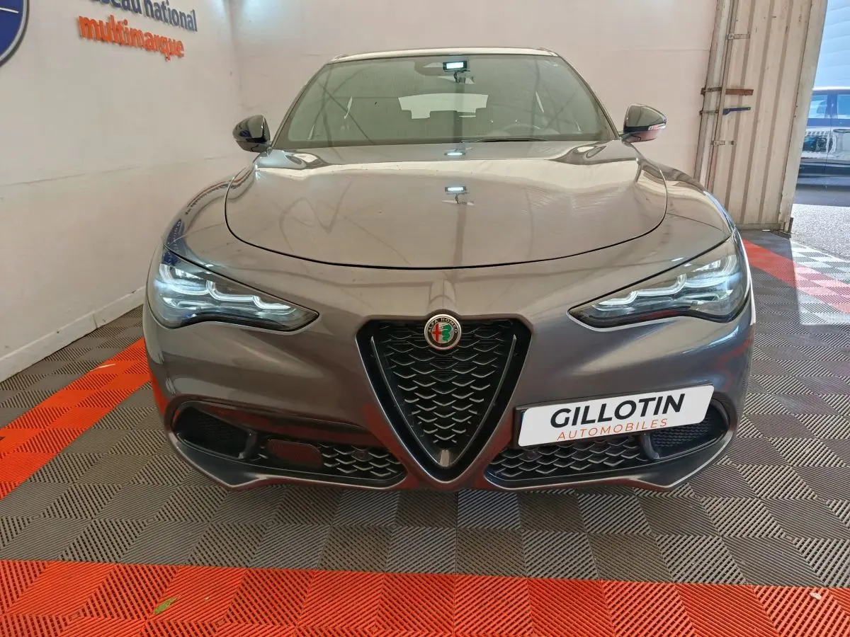 Vue frontale d'un Alfa Romeo Stelvio gris foncé avec calandre triangulaire distinctive et phares LED allumés.