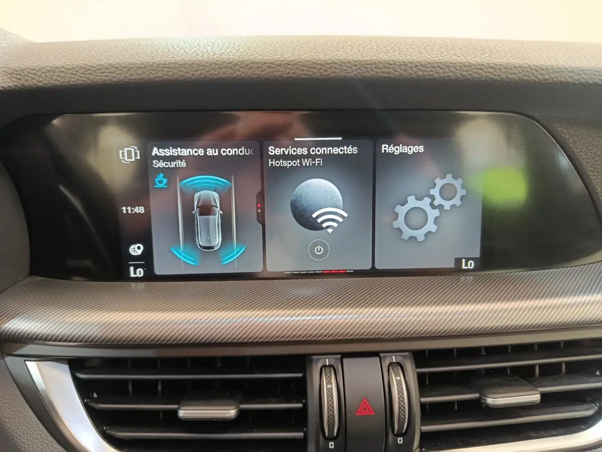 Écran tactile central de l'Alfa Romeo Stelvio 2024 affichant l'assistance conduite, Wi-Fi et réglages, intérieur gris.