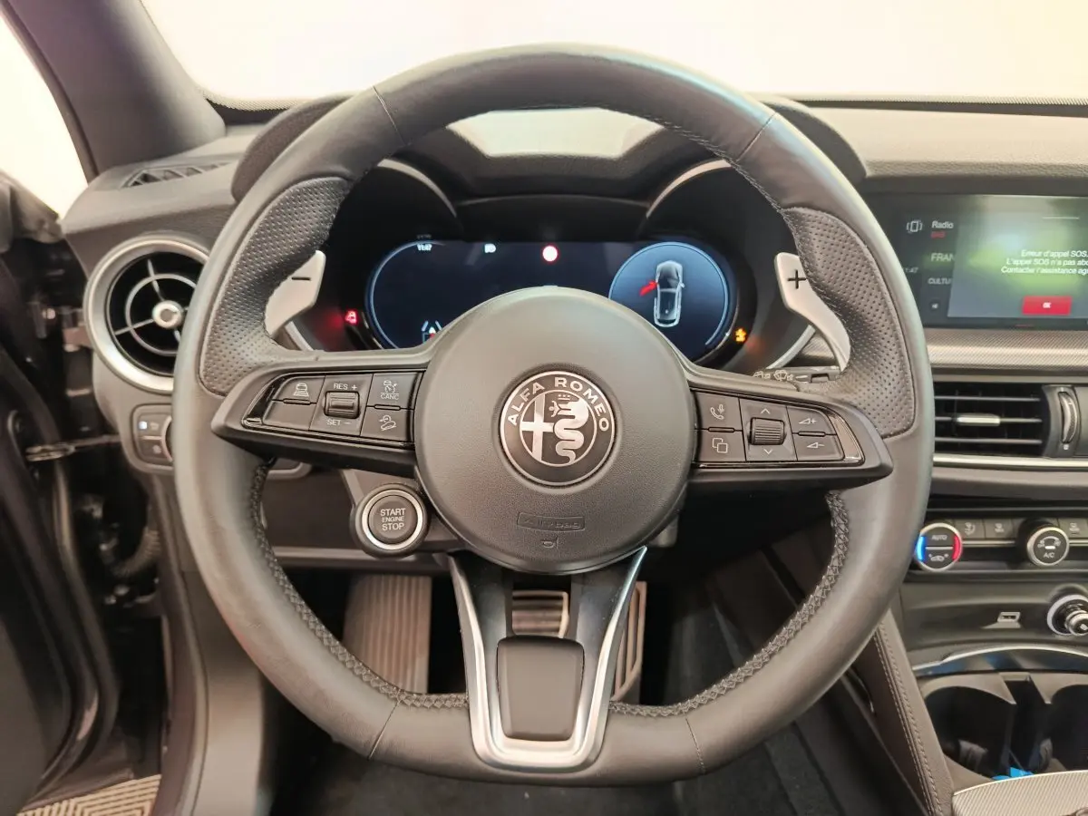 Vue rapprochée du volant cuir noir d'Alfa Romeo Stelvio 2024 avec tableau de bord numérique et bouton start/stop.