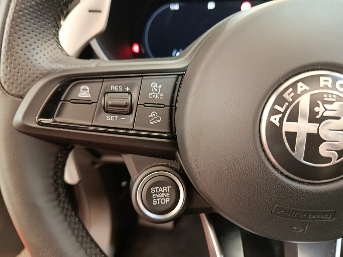 Gros plan sur le volant cuir perforé d’une Alfa Romeo Stelvio 2024 avec boutons de commande et bouton démarrage gris foncé.