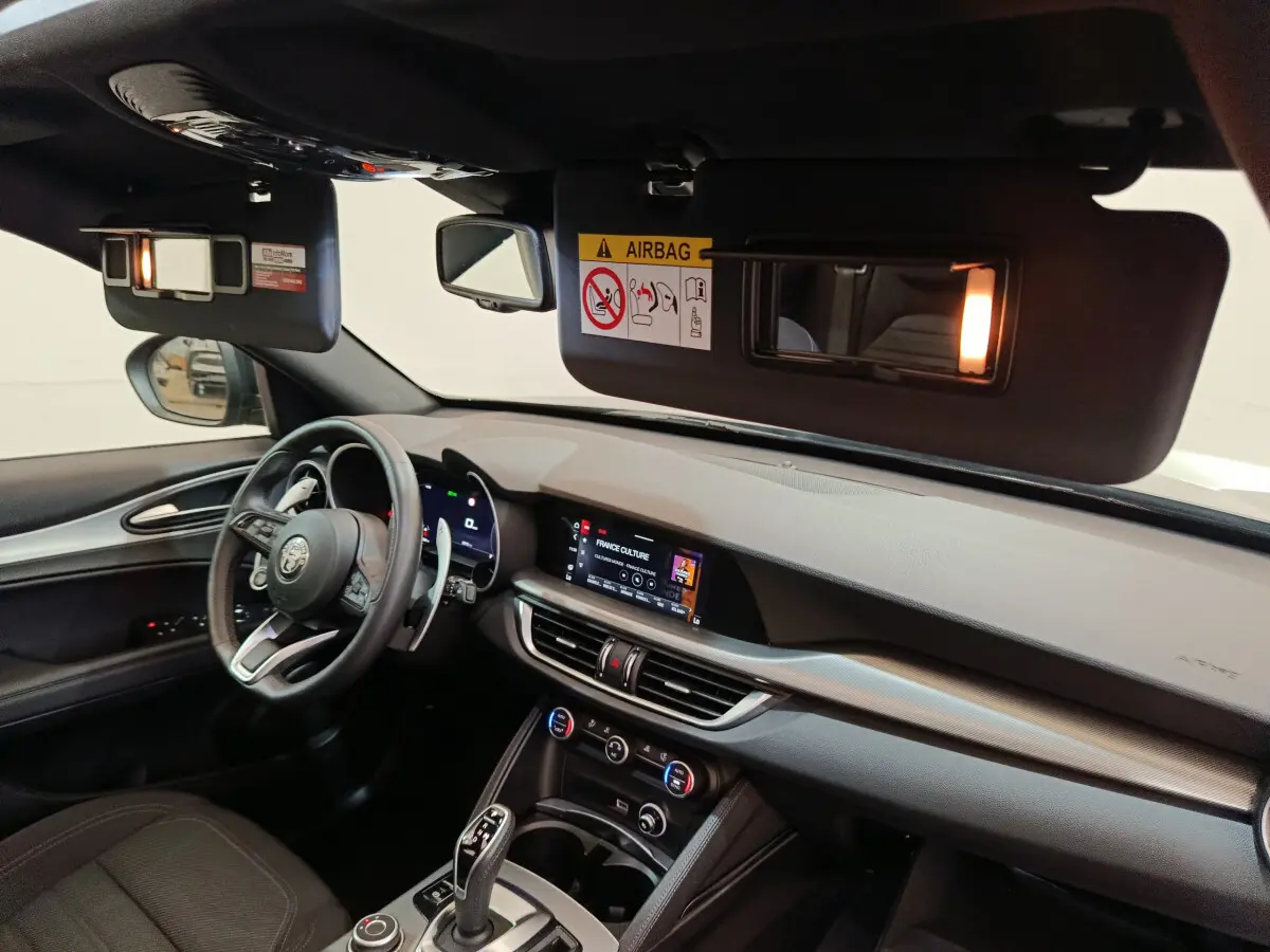 Vue intérieure côté conducteur de l'Alfa Romeo Stelvio gris foncé 2024, avec tableau de bord et écran tactile allumés.