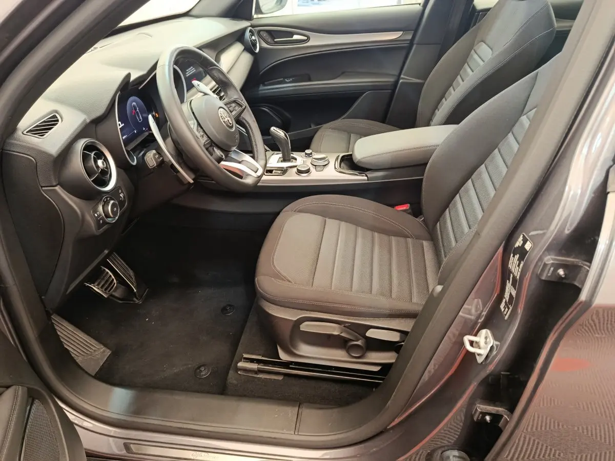 Vue intérieure côté conducteur de l'Alfa Romeo Stelvio gris foncé 2024, avec sièges tissu et tableau de bord moderne.