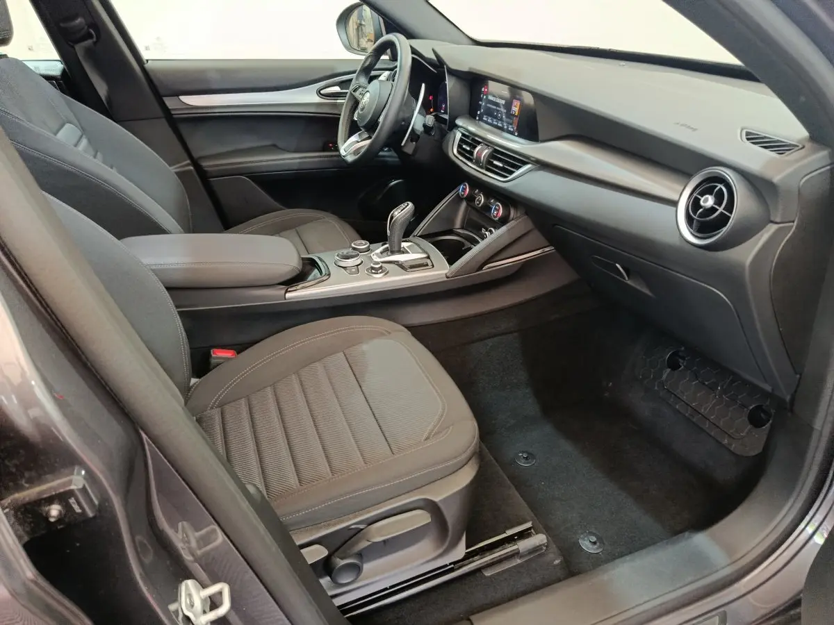 Intérieur côté passager de l'Alfa Romeo Stelvio gris foncé, avec tableau de bord moderne et console centrale épurée.