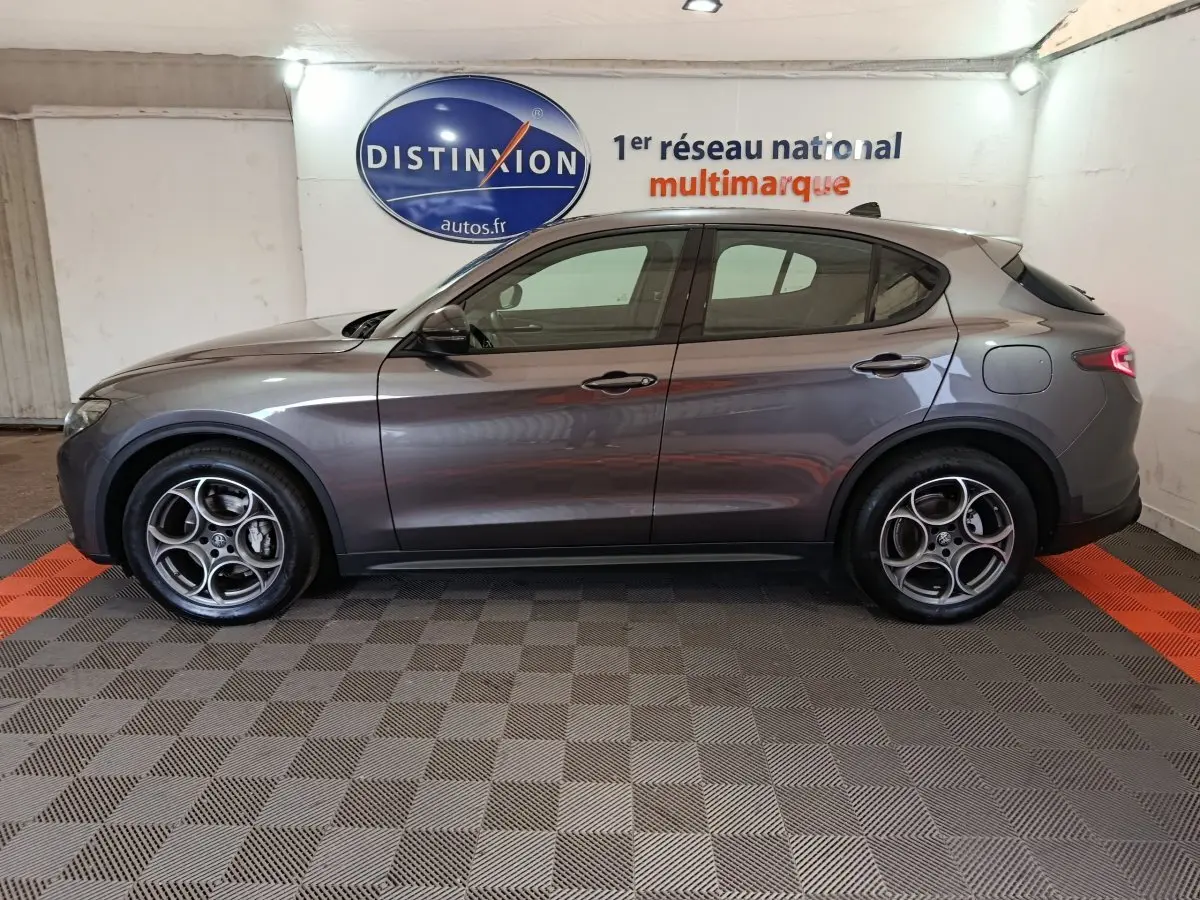 Vue de profil côté gauche d'un Alfa Romeo Stelvio gris foncé 2024 avec jantes distinctives à cinq cercles.
