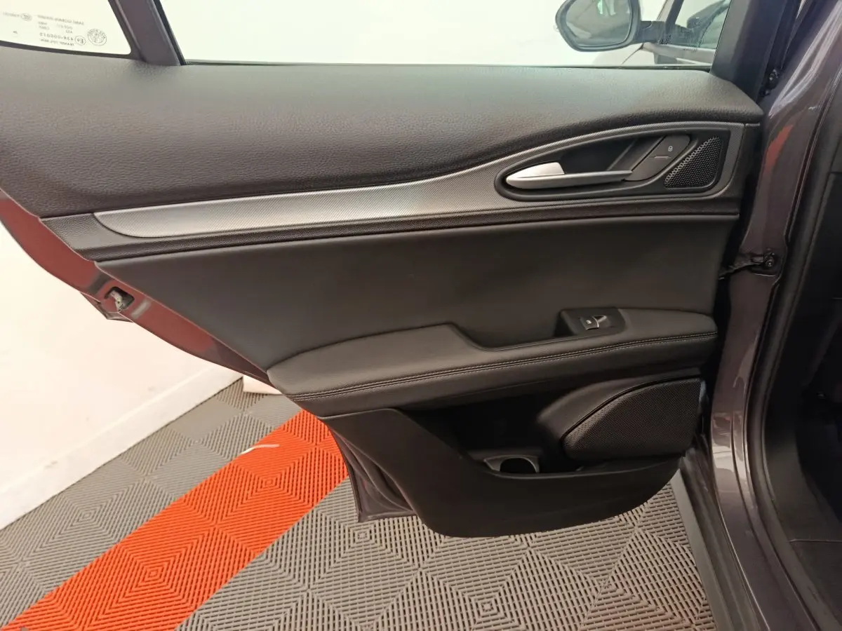 Vue côté gauche de la porte intérieure gris foncé de l'Alfa Romeo Stelvio 2024 avec poignée alu et haut-parleur intégré.