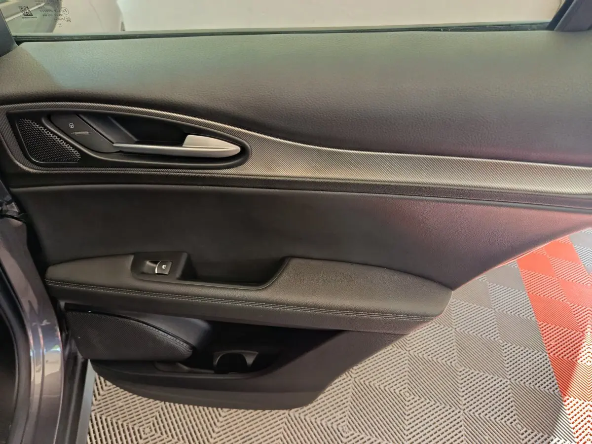 Vue rapprochée de la porte avant gauche de l'Alfa Romeo Stelvio gris foncé, avec poignée argentée et garniture noire.