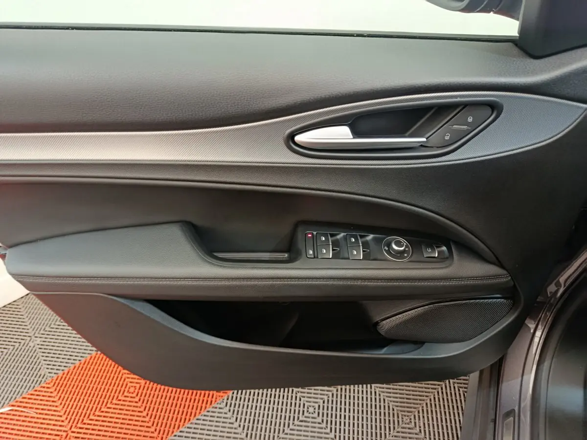 Vue latérale du panneau de porte avant gauche gris foncé d'une Alfa Romeo Stelvio 2024 avec commandes électriques et poignée argentée.