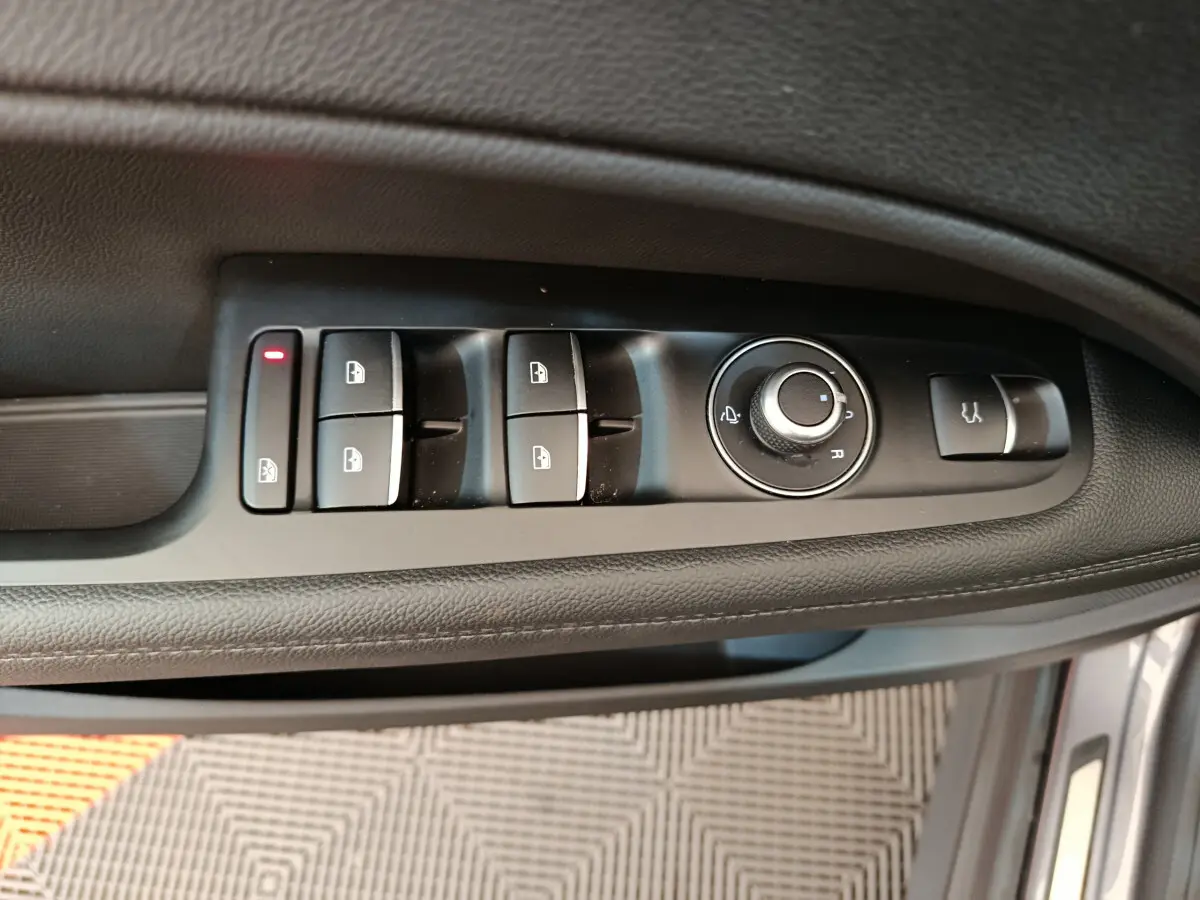 Vue rapprochée des commandes de lève-vitres et rétroviseurs sur la porte côté conducteur d'une Alfa Romeo Stelvio gris foncé.