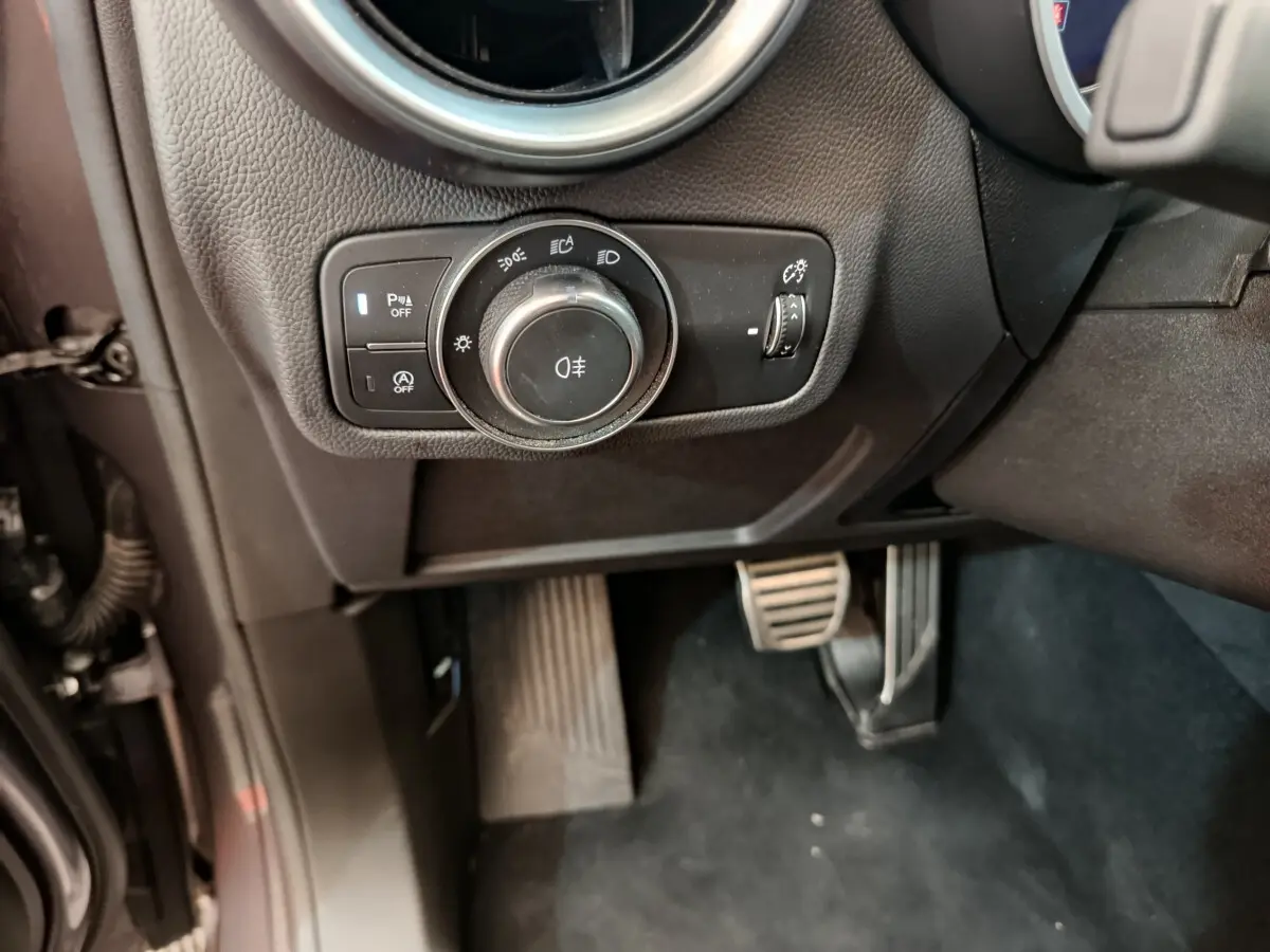 Gros plan sur les commandes d'éclairage et pédales côté gauche de l'Alfa Romeo Stelvio gris foncé 2024.