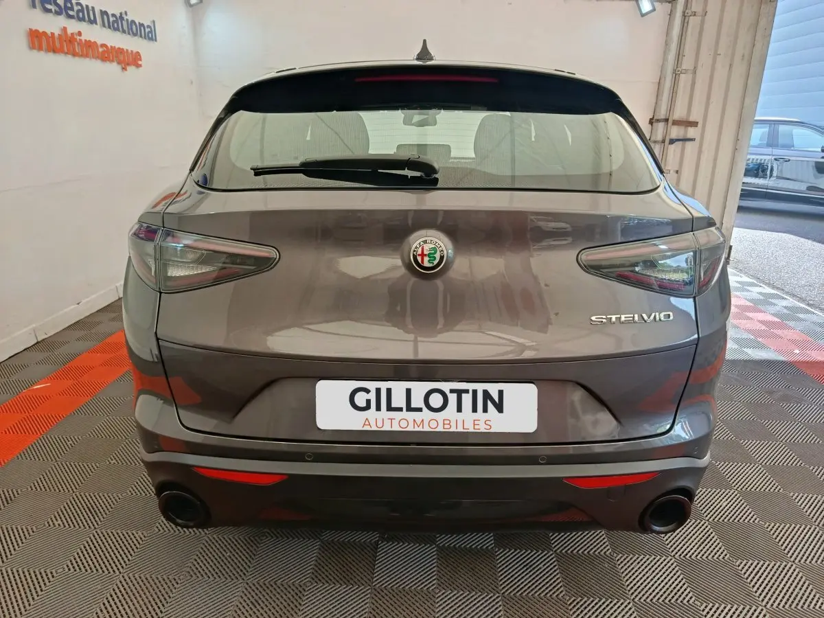 Vue arrière d'un Alfa Romeo Stelvio gris foncé 2024 avec feux LED et double sortie d'échappement noire.