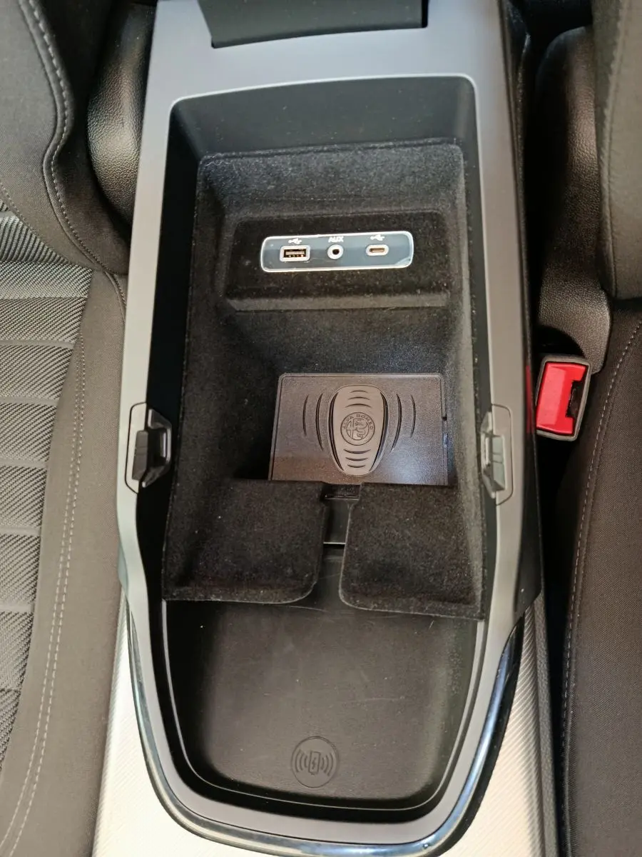 Vue plongeante sur la console centrale noire de l'Alfa Romeo Stelvio 2024 avec ports USB, AUX et zone de recharge sans fil.