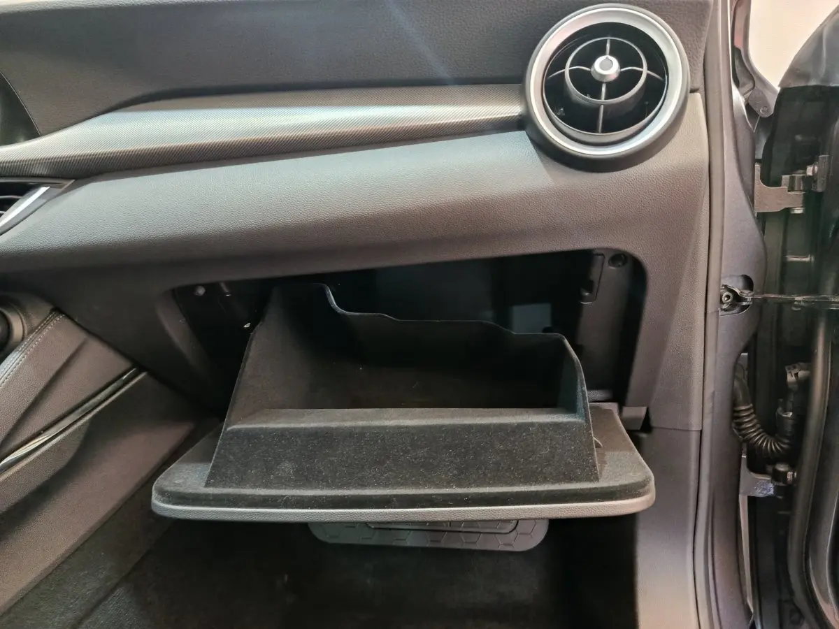 Vue intérieure côté passager de la boîte à gants ouverte de l'Alfa Romeo Stelvio gris foncé, avec aérateur rond visible.