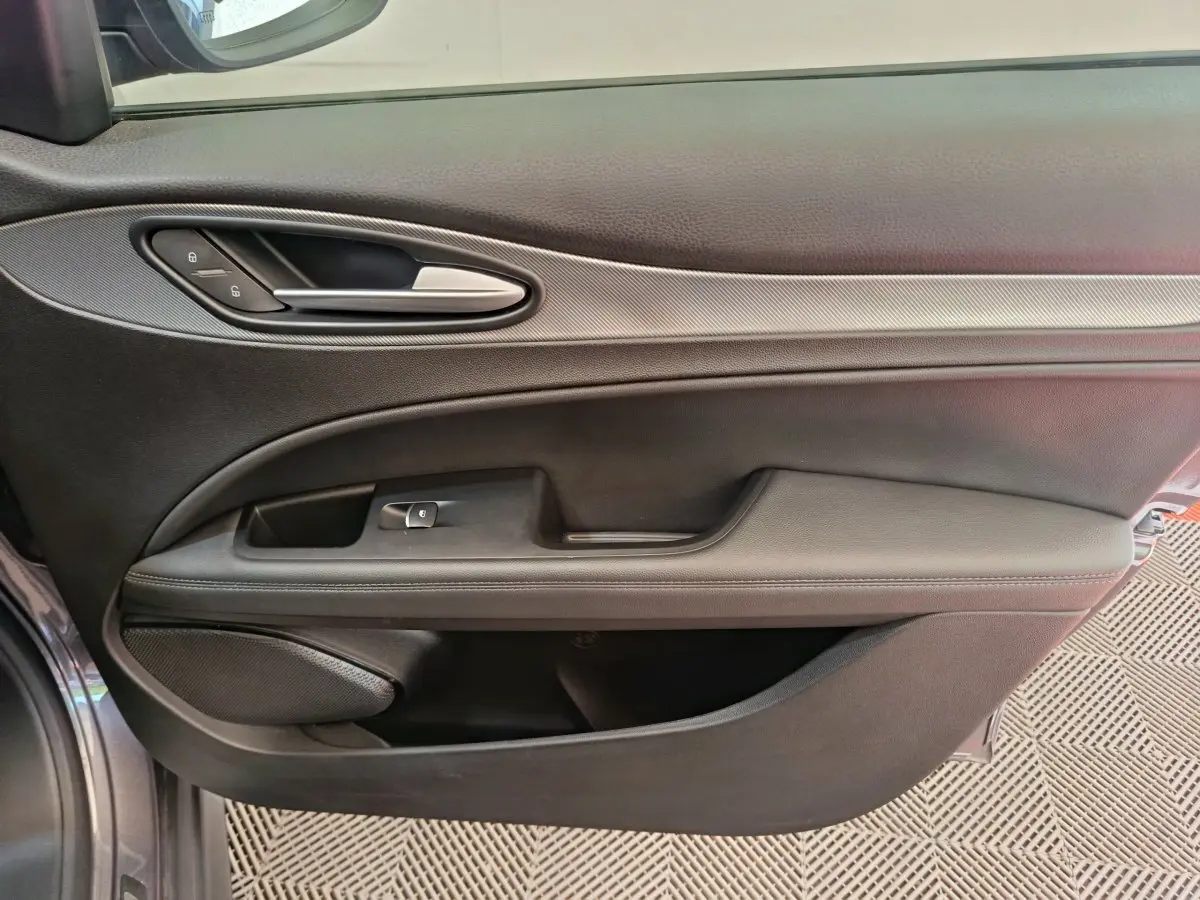Vue intérieure côté gauche de la porte avant gris foncé de l'Alfa Romeo Stelvio avec poignée argentée et commandes de verrouillage.