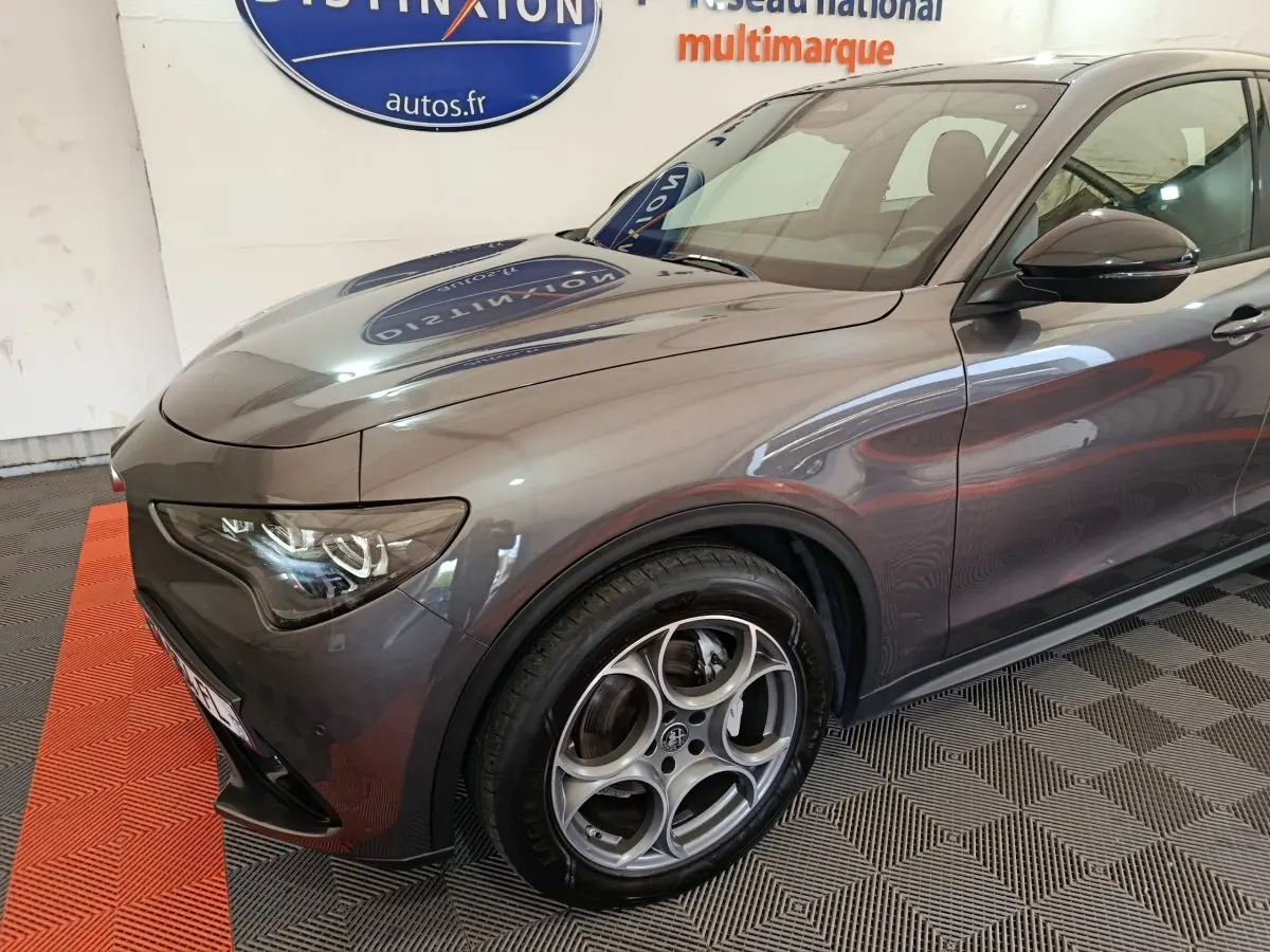 Vue 3/4 avant gauche d’un Alfa Romeo Stelvio gris foncé mettant en valeur ses phares LED et jantes alliage distinctives.