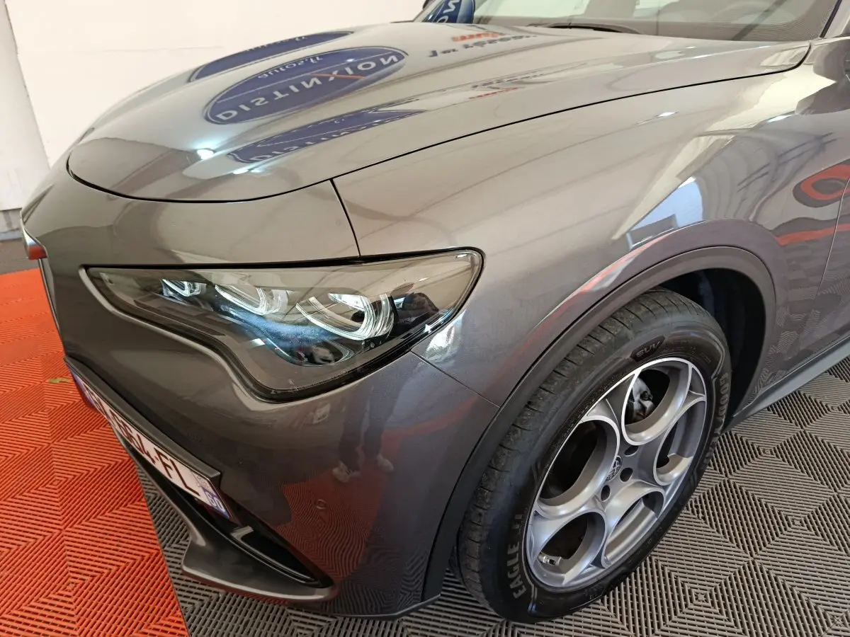 Vue 3/4 avant droit d'un Alfa Romeo Stelvio gris foncé mettant en valeur son phare LED et sa jante distinctive à cinq cercles.